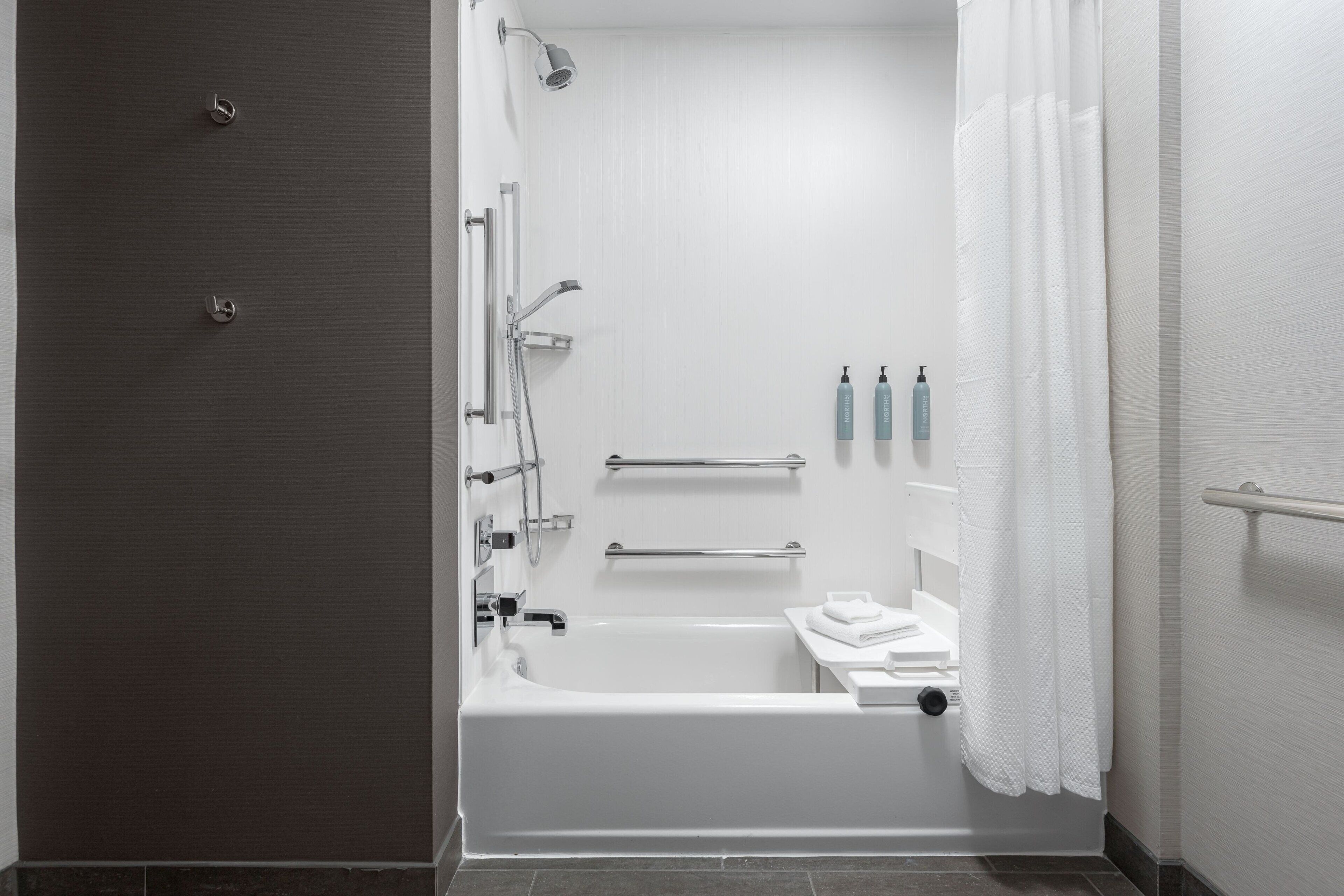 Un baño moderno con bañera, ducha y barras de apoyo.