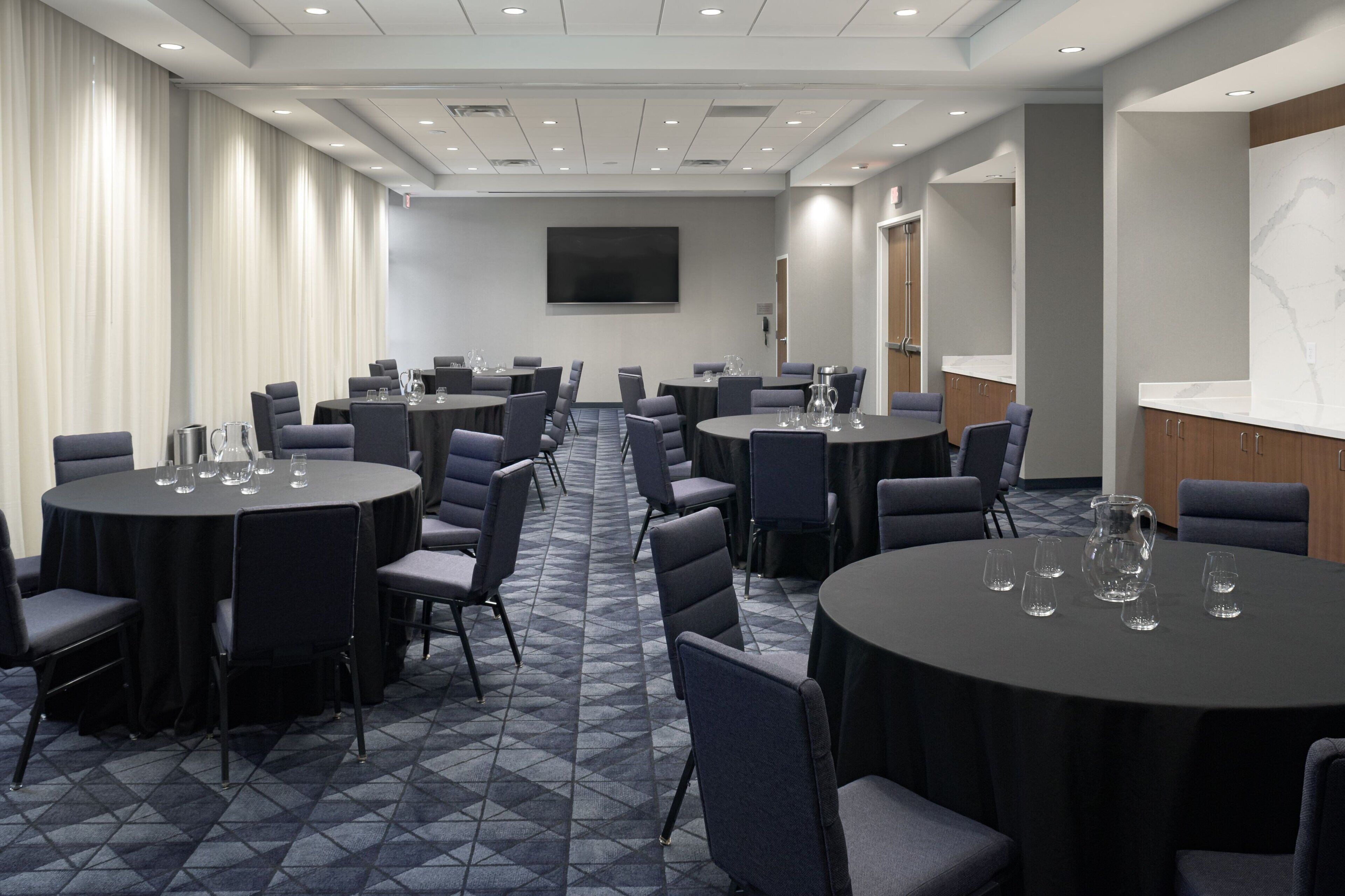 A conference room with multiple round tables, chairs, and a large screen on the wall.
