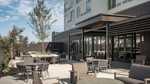 Un patio al aire libre con diversas opciones de mobiliario, incluyendo mesas y sillas, y una zona cubierta con una pérgola.