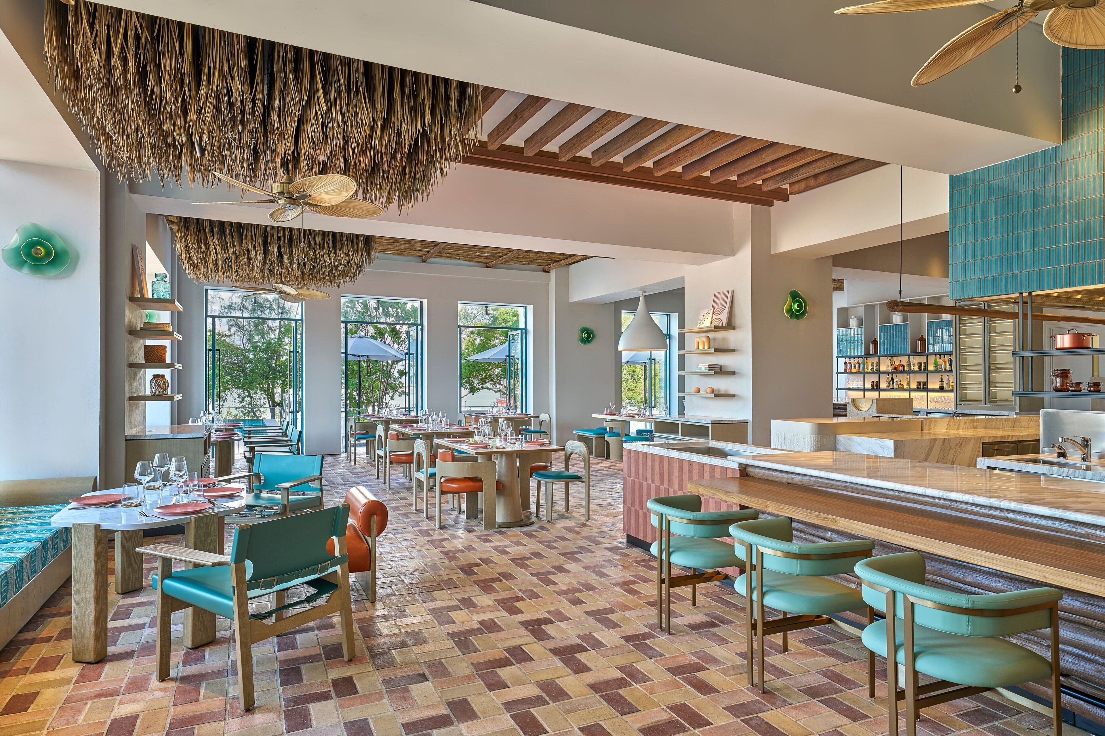 A spacious restaurant with a modern interior, featuring a mix of seating arrangements, a bar area, and large windows providing natural light.