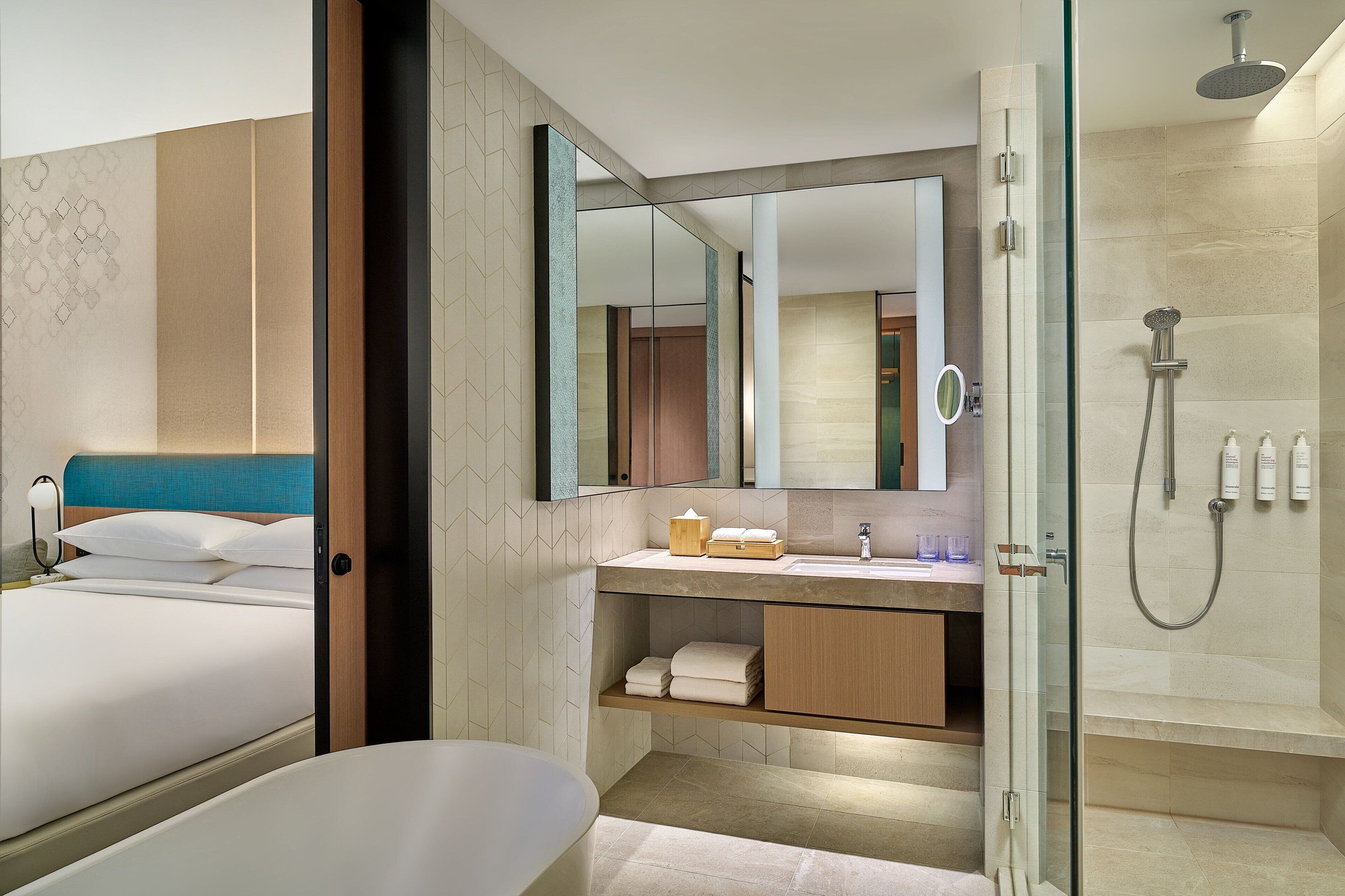 A modern hotel bathroom with a large mirror, a shower, and a bed.