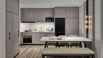 Una cocina moderna con armarios grises, microondas integrado, refrigerador negro y comedor con mesa y sillas.