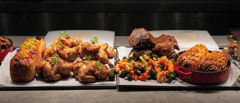 A buffet with various dishes including roasted meats, vegetables, and a whole roasted chicken.