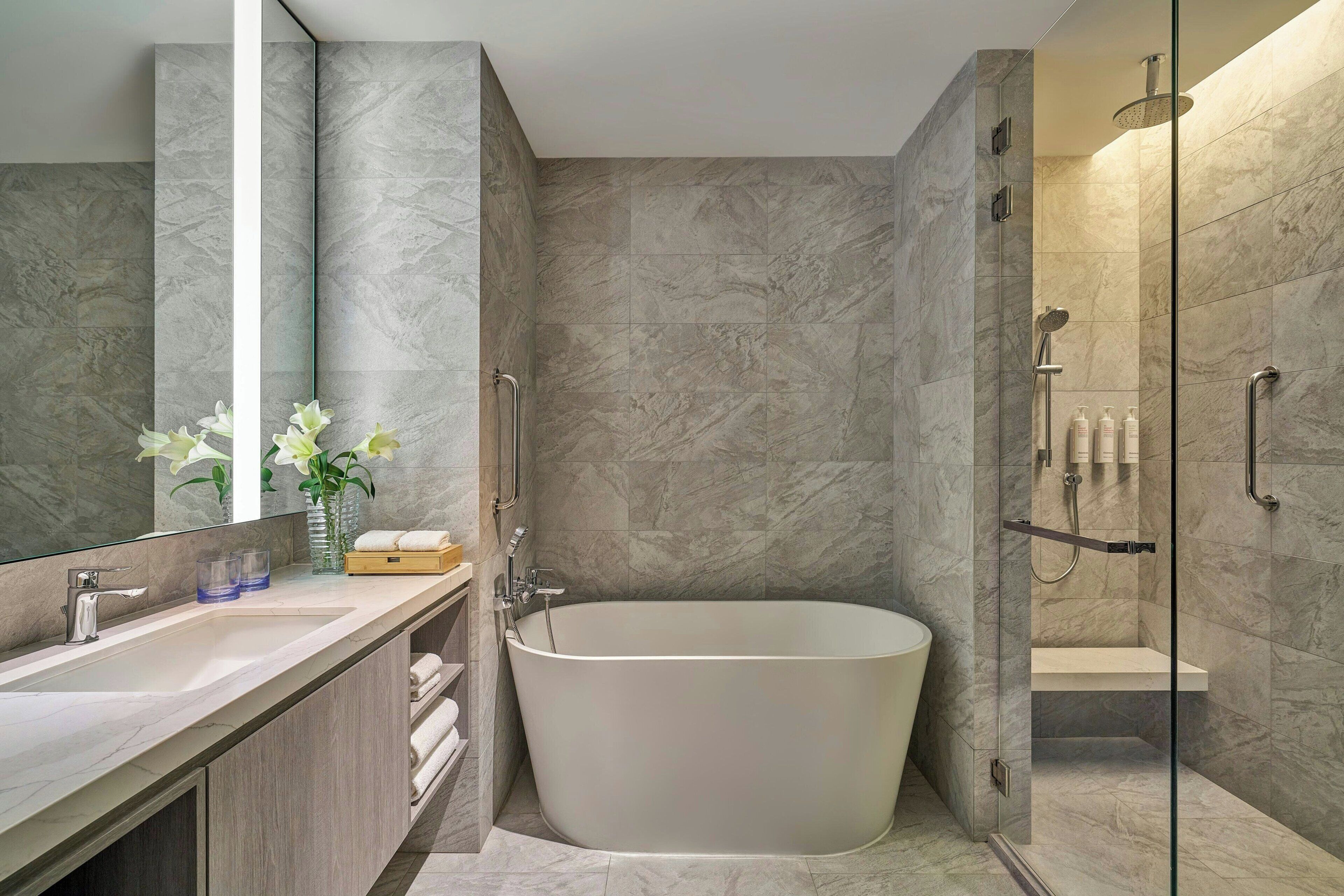 Un baño moderno con una bañera independiente, una ducha con mampara de cristal y un tocador con espejo.