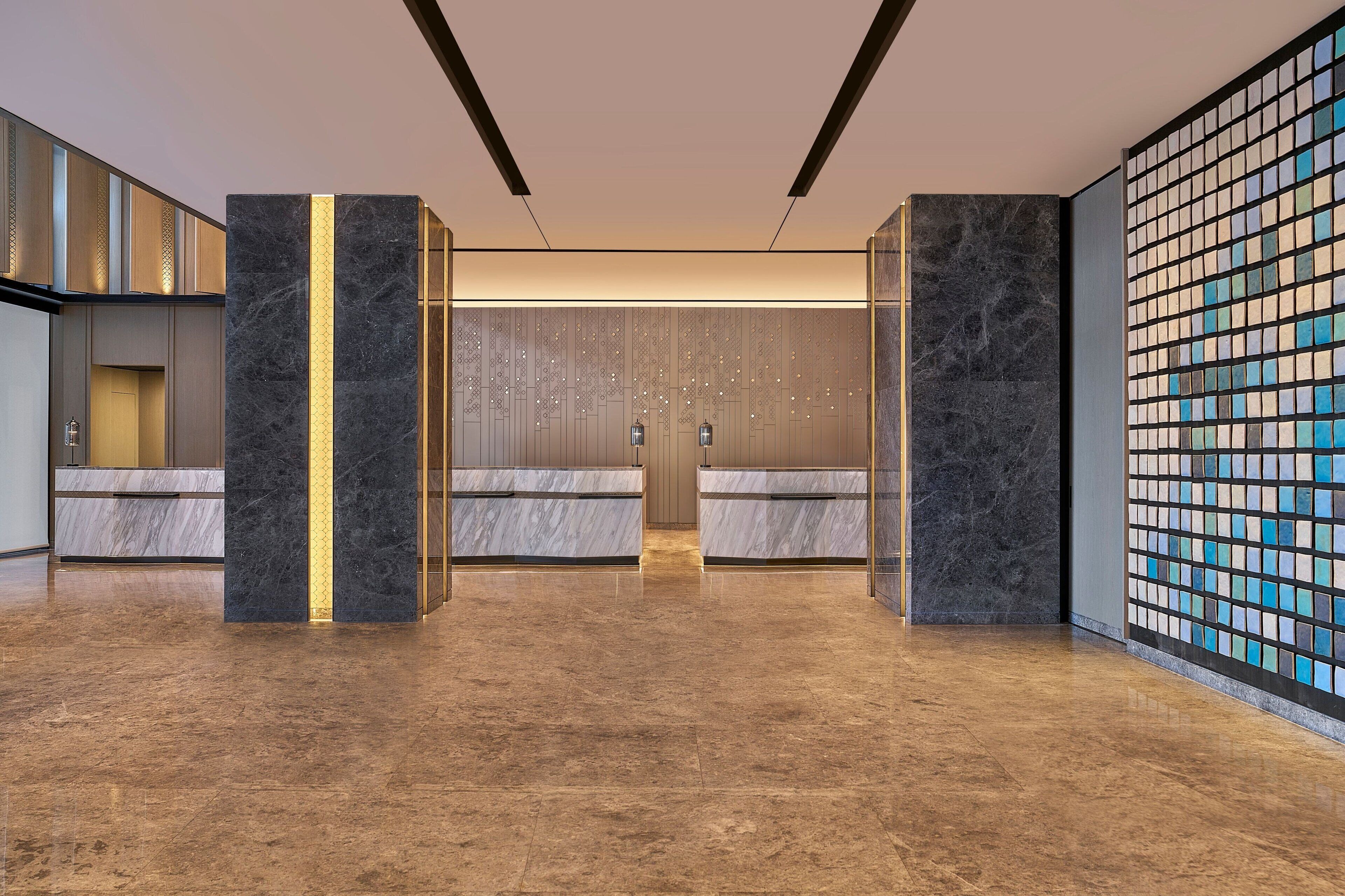 A spacious lobby with marble flooring, a reception desk, and a decorative wall with a mosaic pattern.