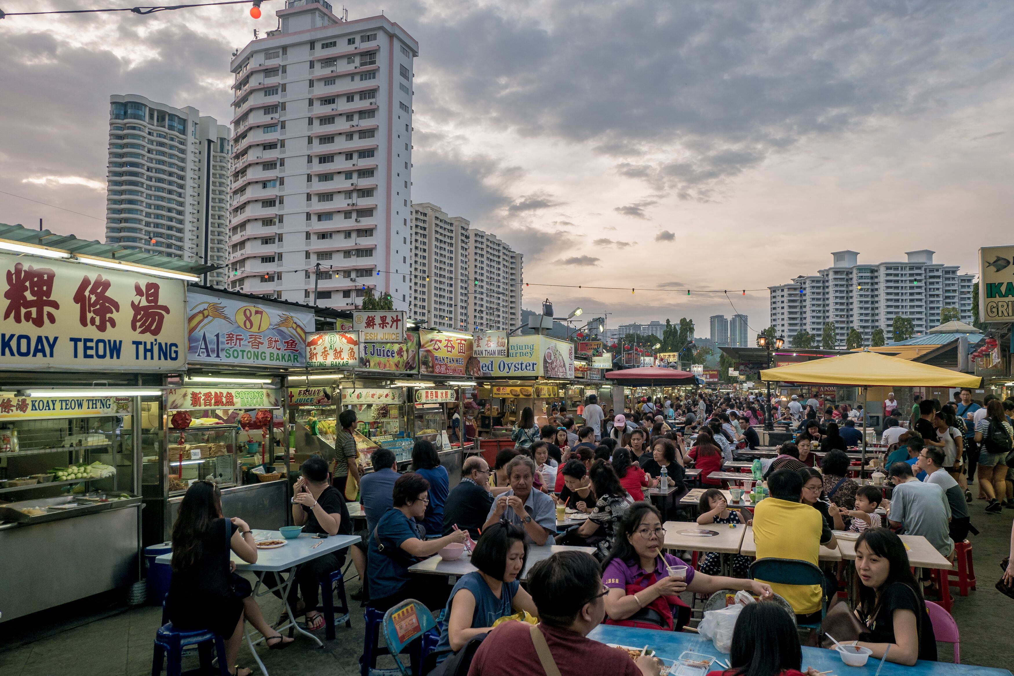 Un mercado animado de comida callejera con varios puestos de comida y una multitud de personas comiendo.