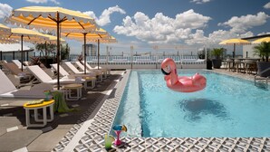 Zona de piscina con sillas de descanso, sombrillas y un flotador con forma de flamenco rosa.