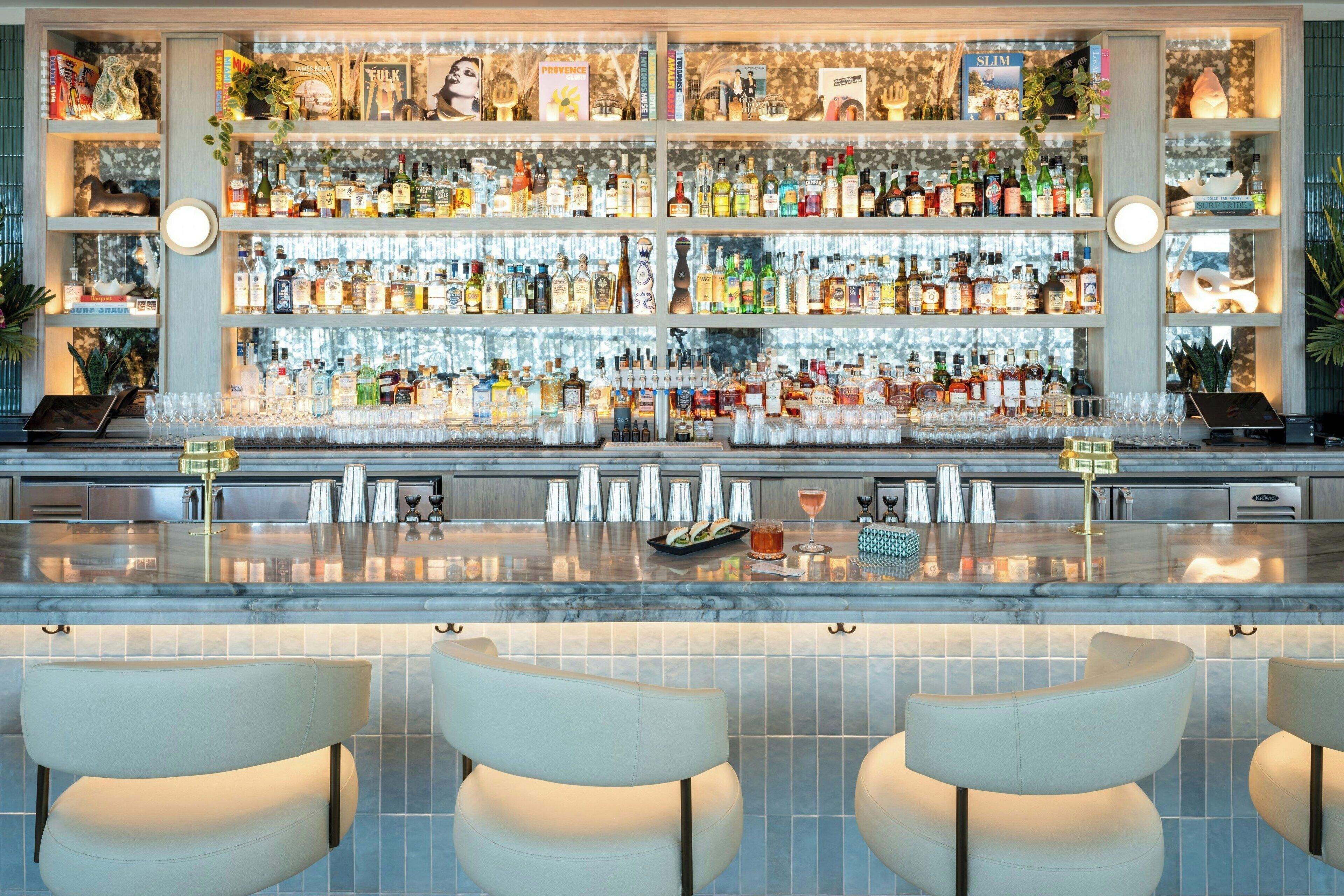 A bar area with multiple shelves of liquor bottles, a marble countertop, and three bar stools.