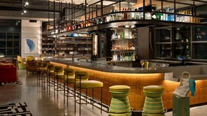 Zona de bar moderna con una barra curva, varios taburetes y una selección de botellas en estantes.