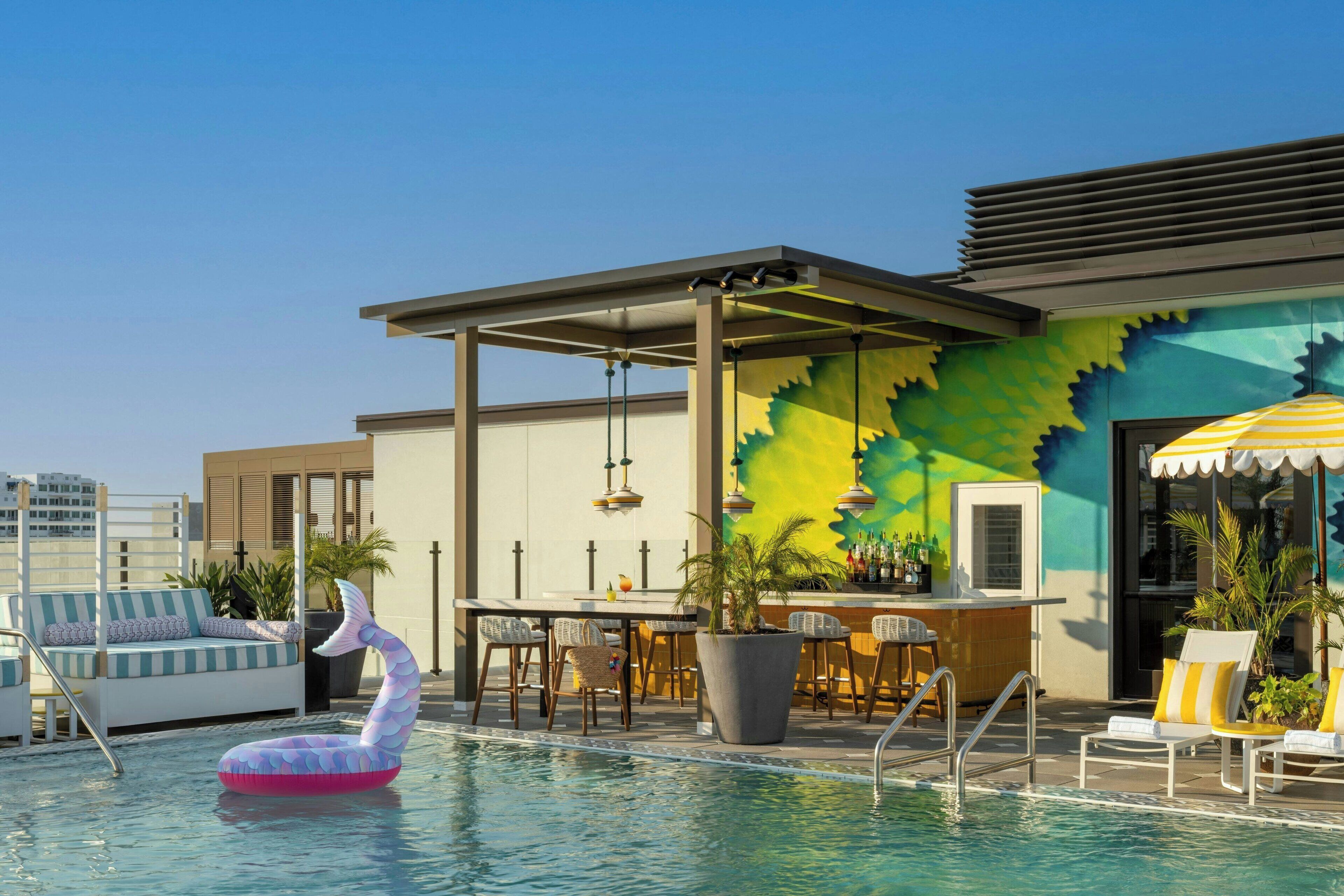 A rooftop pool area with lounge chairs, a bar, and a colorful mural.