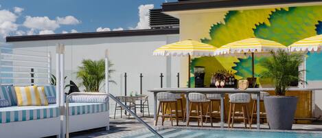 Zona de piscina con bar, asientos y sombrillas.