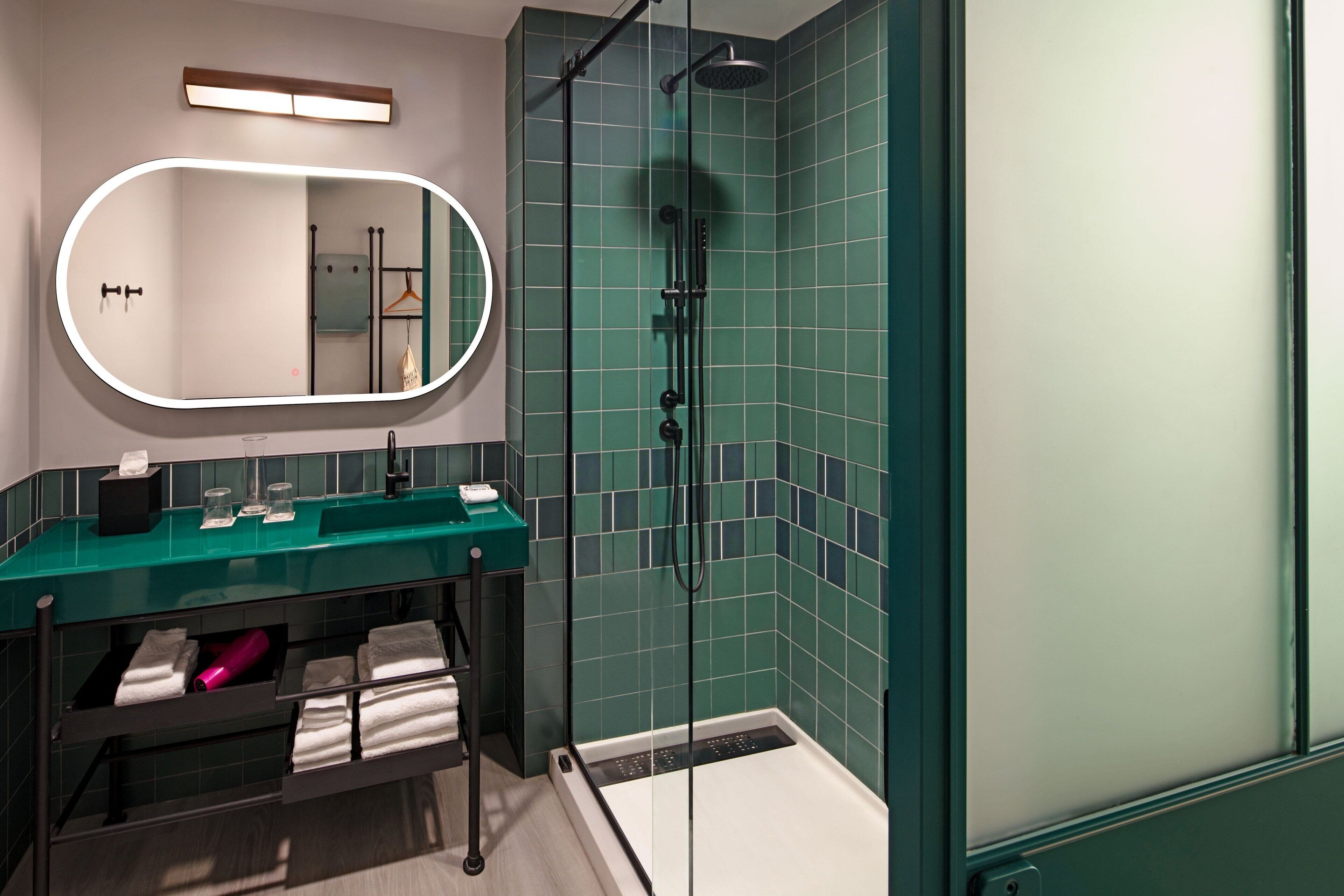 Un baño moderno con ducha envuelta en vidrio, tocador con cubierta verde y un espejo grande.