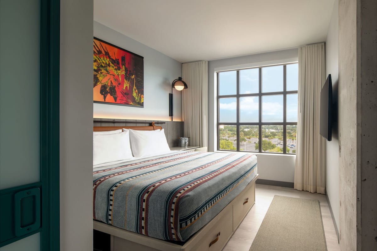 Ein modernes Hotelzimmer mit einem großen Bett, Blick auf die Stadt, einem Flachbildfernseher und einem Gemälde an der Wand.