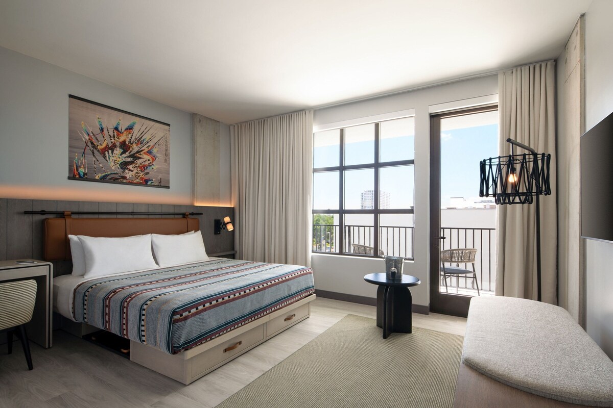 Une chambre d’hôtel moderne dotée d’un grand lit, d’un bureau, d’une chaise, d’un balcon avec vue et d’un élément décoratif mural.