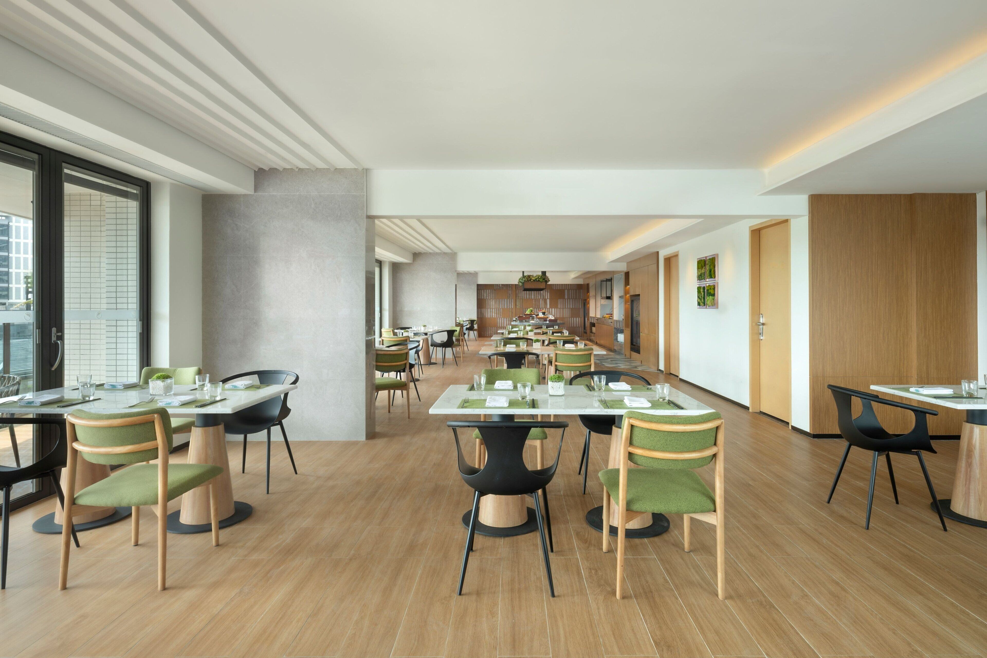 Uma ampla sala de jantar com várias mesas e cadeiras, um design moderno no teto e vista da cidade através de grandes janelas.