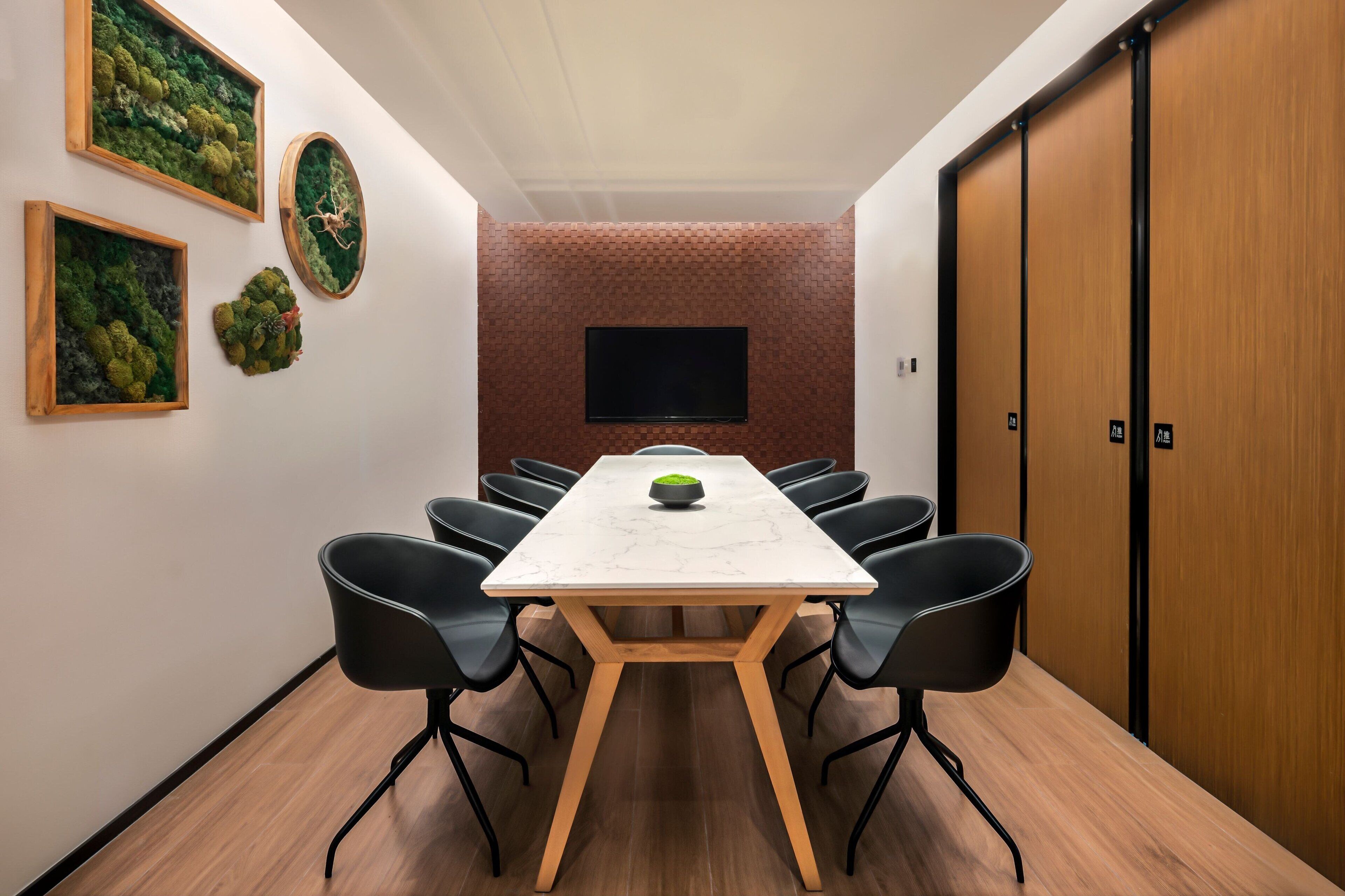 Uma sala de conferência com uma mesa comprida, cadeiras pretas, uma televisão na parede e uma porta de madeira.