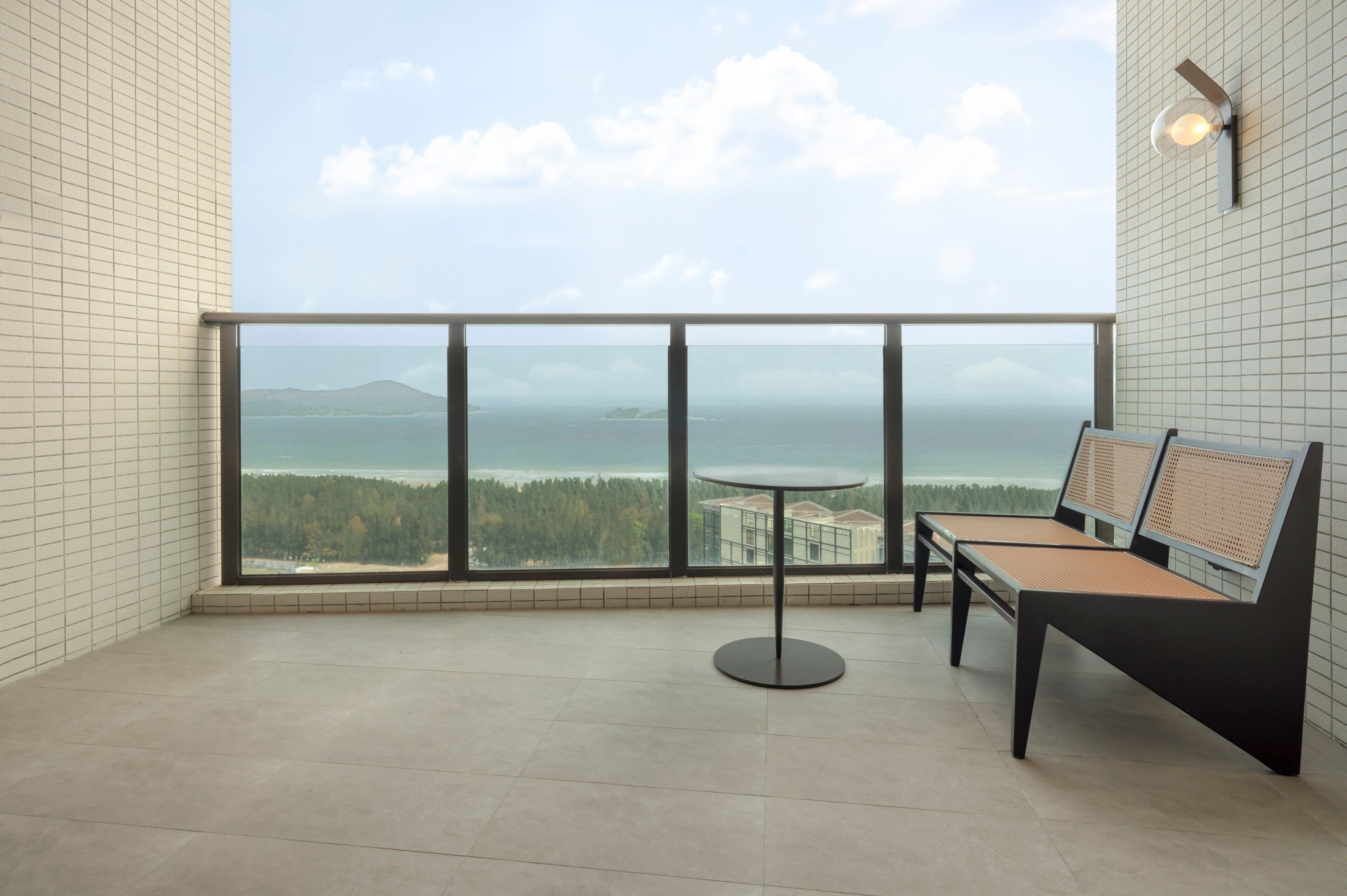 A balcony with a view of the sea and a distant island, featuring a round table and two chairs.