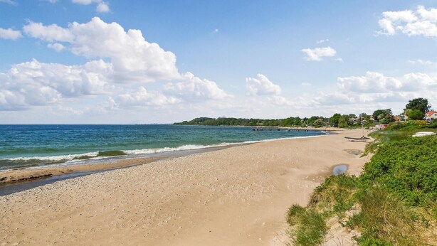 A beach with a clear sky, calm sea, and a distant shoreline with greenery and buildings. - 3 bedroom stunning home in Ystad (Ystad)
