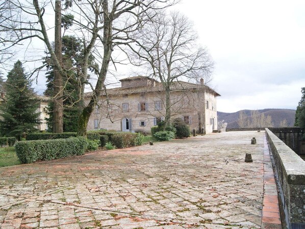 A historic stone building with a courtyard, surrounded by mature trees and a stone wall. - Belvilla by OYO Casa Sequoia (Rufina)