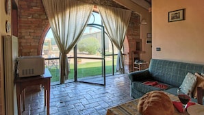 A cozy living room with a stone wall, a wooden table with a loaf of bread and a wine glass, and a green sofa. - Cottage in Todi with Pool and Terrace (Todi)