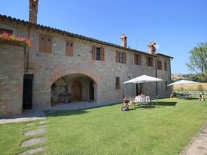 A stone building with a courtyard, outdoor seating, and a grassy area. - Apartment in Todi with Pool & History (Todi)
