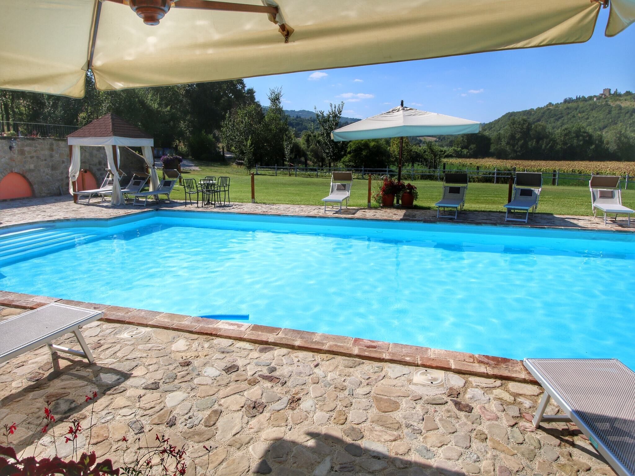 A swimming pool with lounge chairs and umbrellas, surrounded by stone walls and greenery.