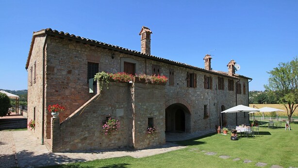 A stone building with a tiled roof, arched windows, and a small tower. There are potted plants and a table with chairs outside. - Apartment in Todi with Pool and Garden (Todi)