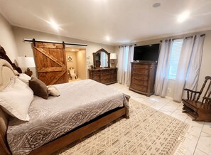 A bedroom with a bed, a wooden wardrobe, a dresser, a television, and a large mirror. - The Magnolia on Critz • Private Pool • Upscale Stay Near MSU (Starkville)