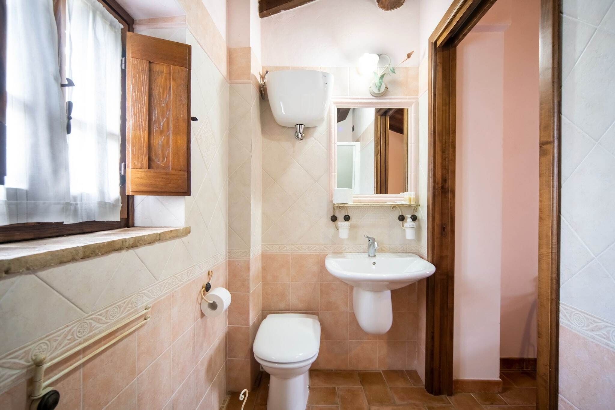 A bathroom with a toilet, sink, and window with curtains.