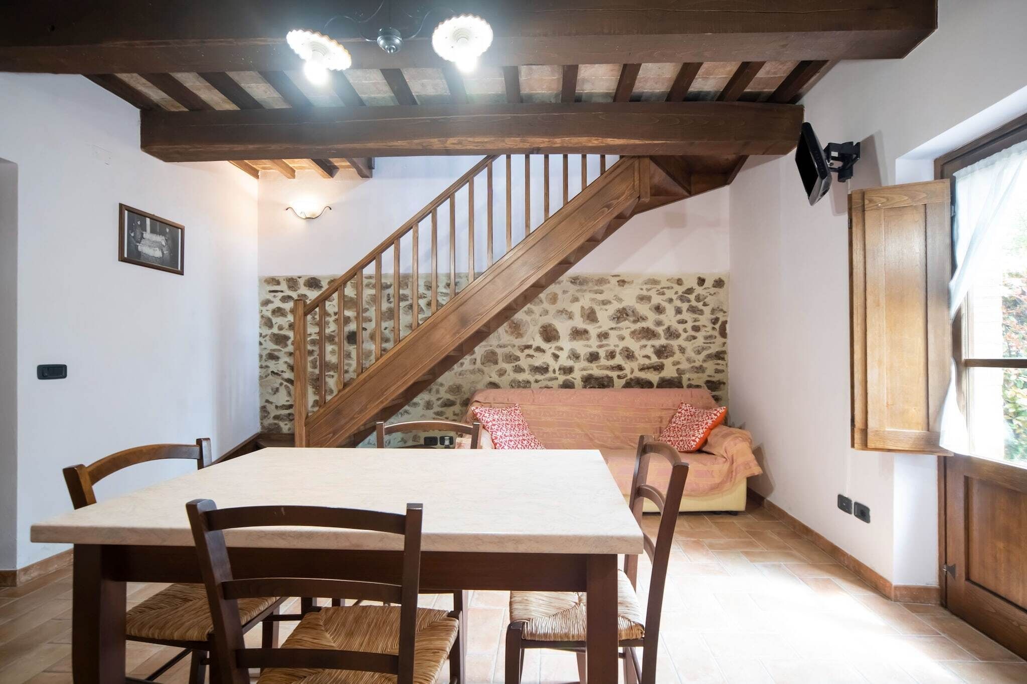 Ein Essbereich mit Holztisch und Stühlen, einer Steinwand, einer Treppe und einem Fenster mit Vorhängen.