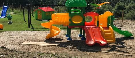 Un parque infantil con tobogán, estructuras de escalada y una casita.