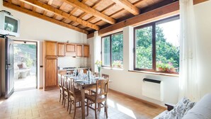 A spacious kitchen with wooden cabinets, a dining table set for six, and large windows offering a view of greenery. - Farmhouse in Marche with Panoramic Views (Apecchio)