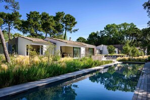 Una casa moderna con piscina, rodeada de árboles y vegetación.