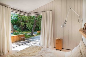 Un dormitorio con un ventanal grande, una mesita de noche, una lámpara y vistas al exterior.