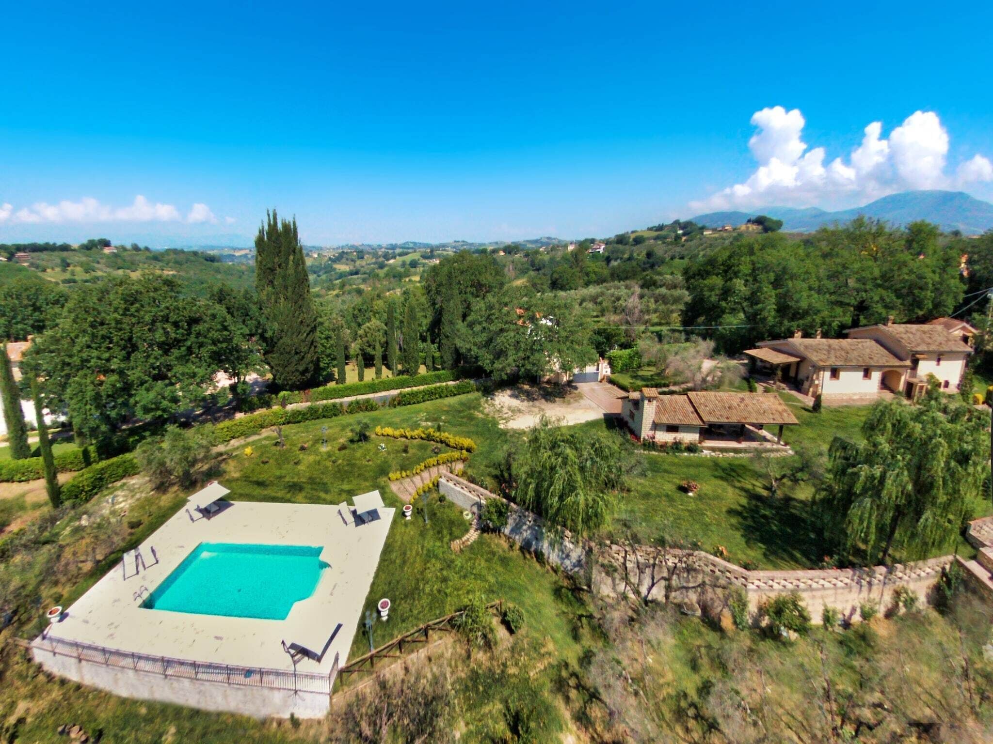 A villa with a swimming pool surrounded by lush greenery and hills in the background.