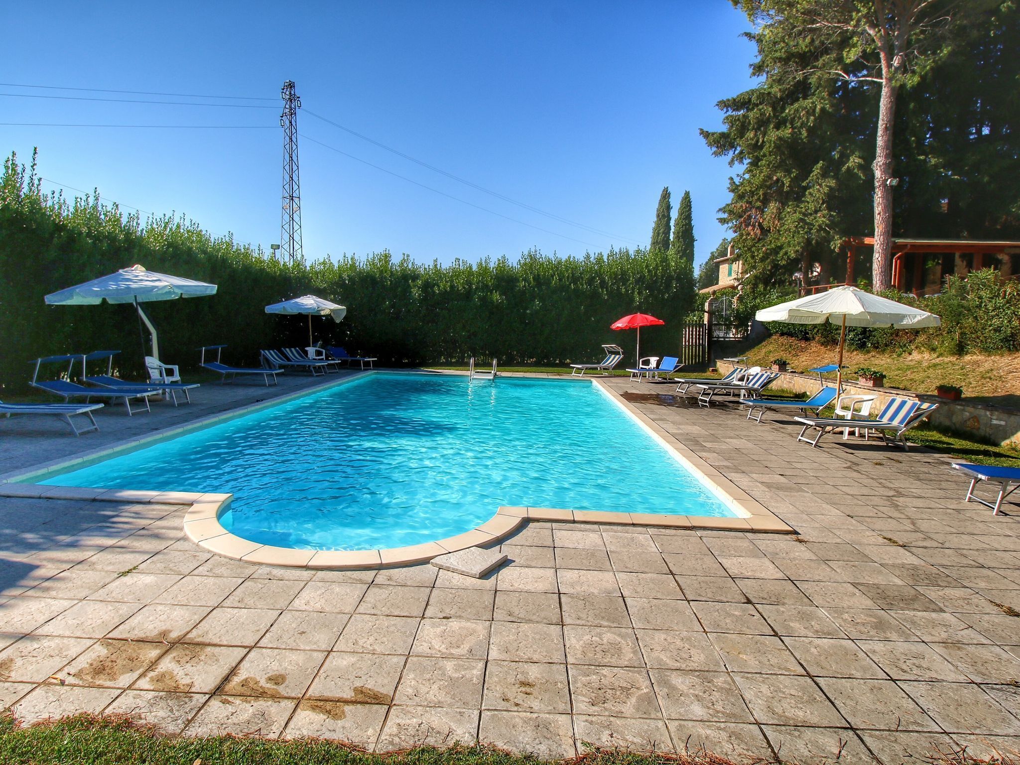 Ein rechteckiger Swimmingpool mit einer gefliesten Liegefläche, umgeben von Liegestühlen und Sonnenschirmen.