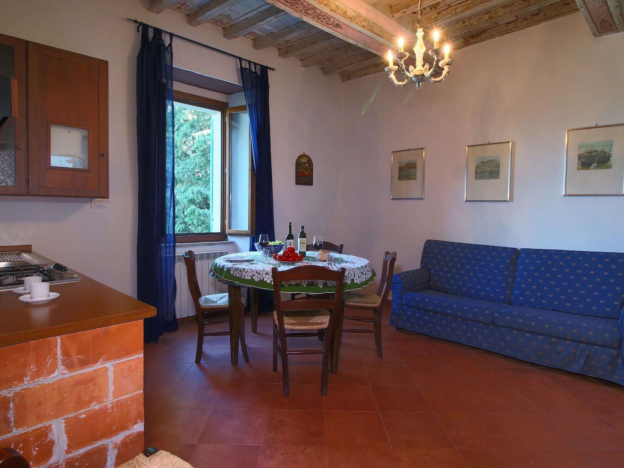 A dining area with a round table, chairs, a blue sofa, and a kitchen with a gas stove.