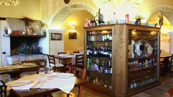 Un accogliente ristorante con camino, tavoli in legno e un'area bar con diverse bottiglie.