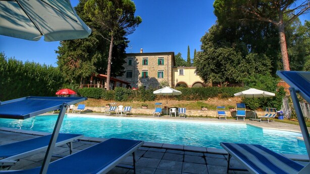 A pool area with lounge chairs and umbrellas, surrounded by trees and a stone building. - Farmhouse in Umbria near Lake Trasimeno (Gualdo Cattaneo)