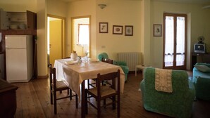 Un'area pranzo con un tavolo apparecchiato per due, una poltrona verde, un tavolino con un vaso e un televisore su un mobile.