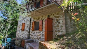 Un edificio in pietra con un balcone, persiane di legno e un piccolo spazio esterno con posti a sedere.