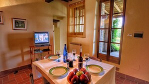 Un coin repas avec une table dressée pour quatre personnes, un téléviseur et une fenêtre donnant sur un paysage verdoyant.