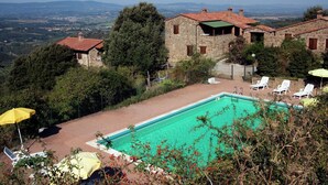 Una villa de piedra con piscina, rodeada de exuberante vegetación y con vistas a colinas distantes.