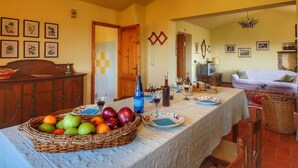 Un comedor con una mesa dispuesta para cuatro, una cesta de mimbre con fruta y un televisor al fondo.