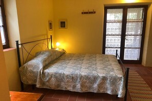Een enkel bed met een bedsprei met patroon in een kamer met een raam, een wandplank en een klein tafeltje.