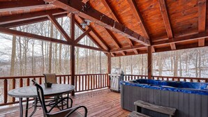 A wooden deck with a hot tub, barbecue grill, and a table with chairs.