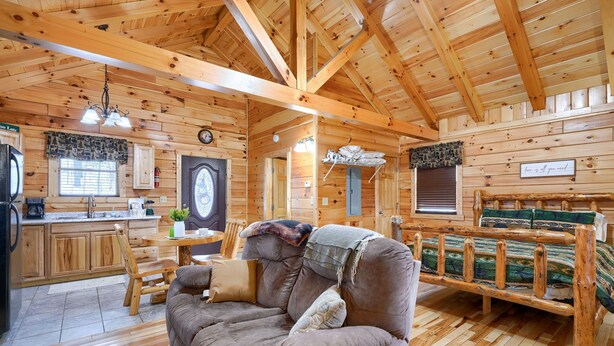 A cozy cabin interior with a wooden ceiling, a dining area, a sofa, and a bed.