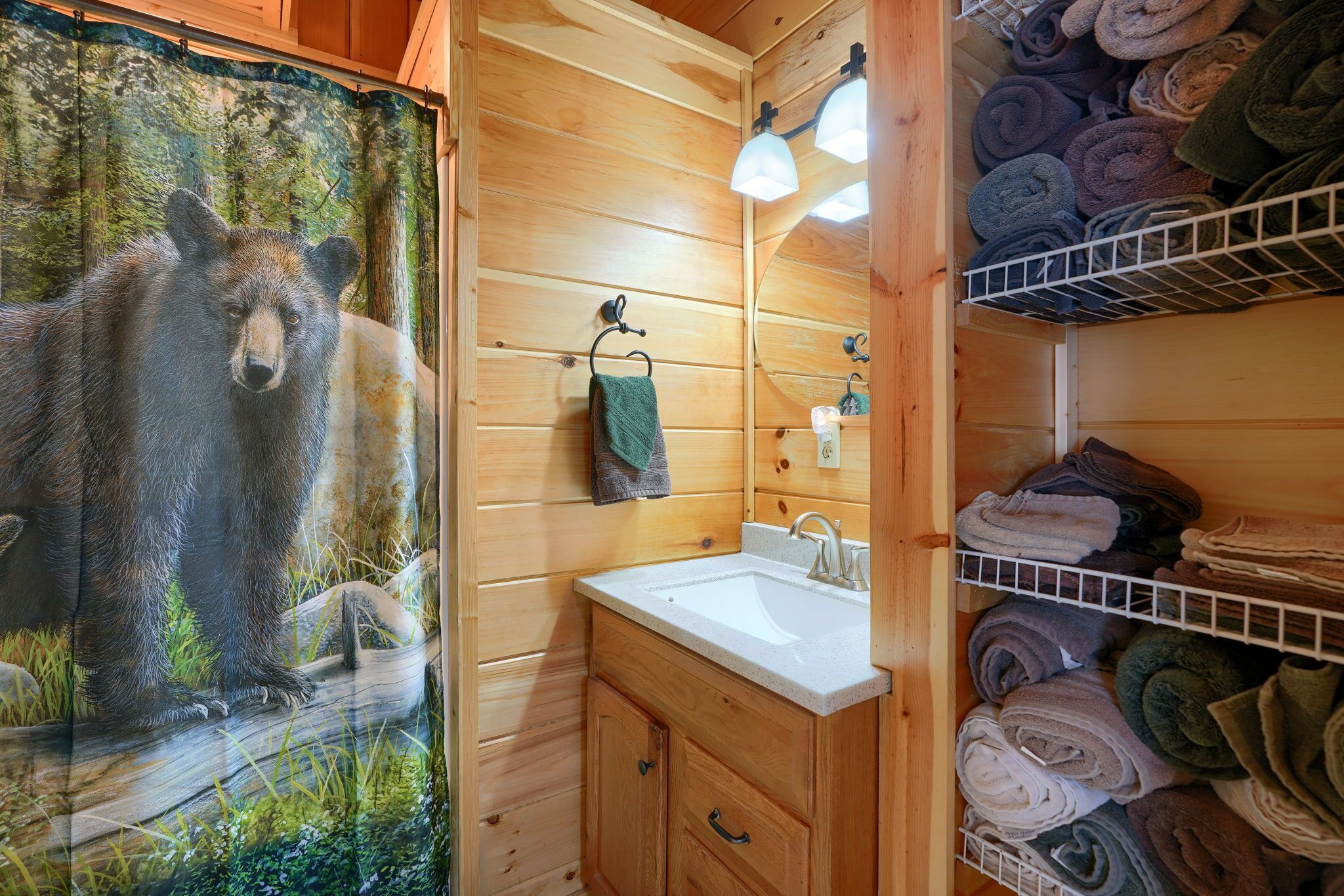 Une salle de bain rustique, aménagée dans une cabane en bois, avec une fresque représentant un ours, un lavabo et des étagères où sont rangées des serviettes pliées.