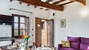 A dining area with a wooden table set for four, a purple sofa, and a kitchen visible through an open door. - Cottage in Magione near Lake Trasimeno (Magione)