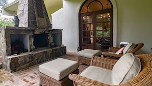 A stone fireplace with two cushioned chairs and a wicker ottoman in a covered outdoor area. - Boquete Luxury: Chic & Serene Home, Walk to Town & Amenities (Boquete)